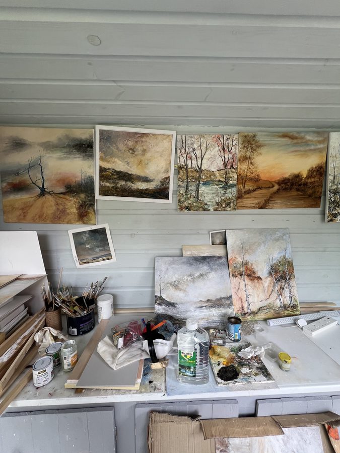 Finished paintings propped and hung along the studio wall above a paint-covered bench